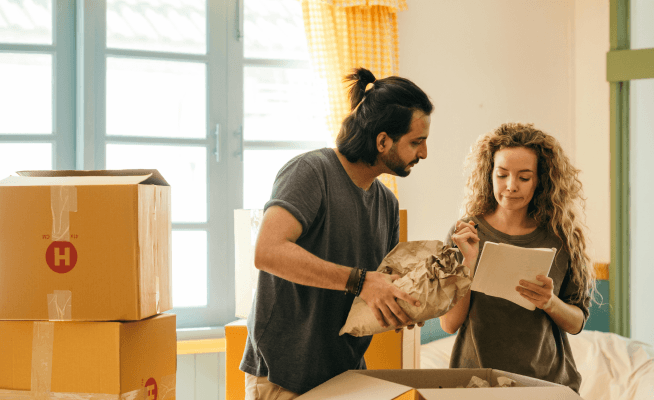 A man and woman carrying boxes into a room, helping each other with the move.