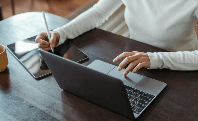 A woman sitting at a table, using a laptop and pen.