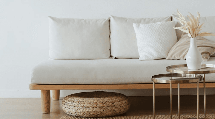 A white couch with pillows and a vase on a wooden floor in a living room.